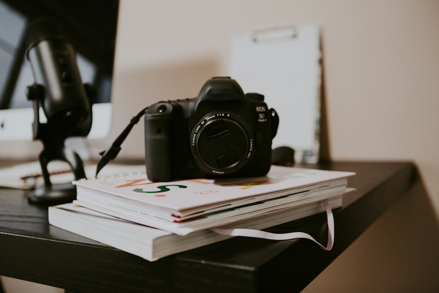 Black camera resting on notebooks with a pink ribbon.