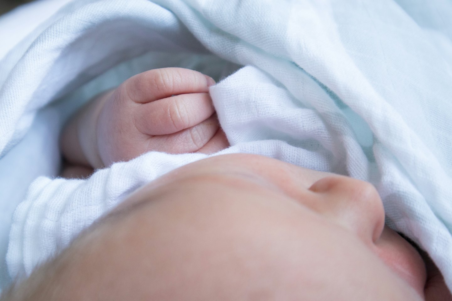 A newborn baby wrapped in white and blue blankets.