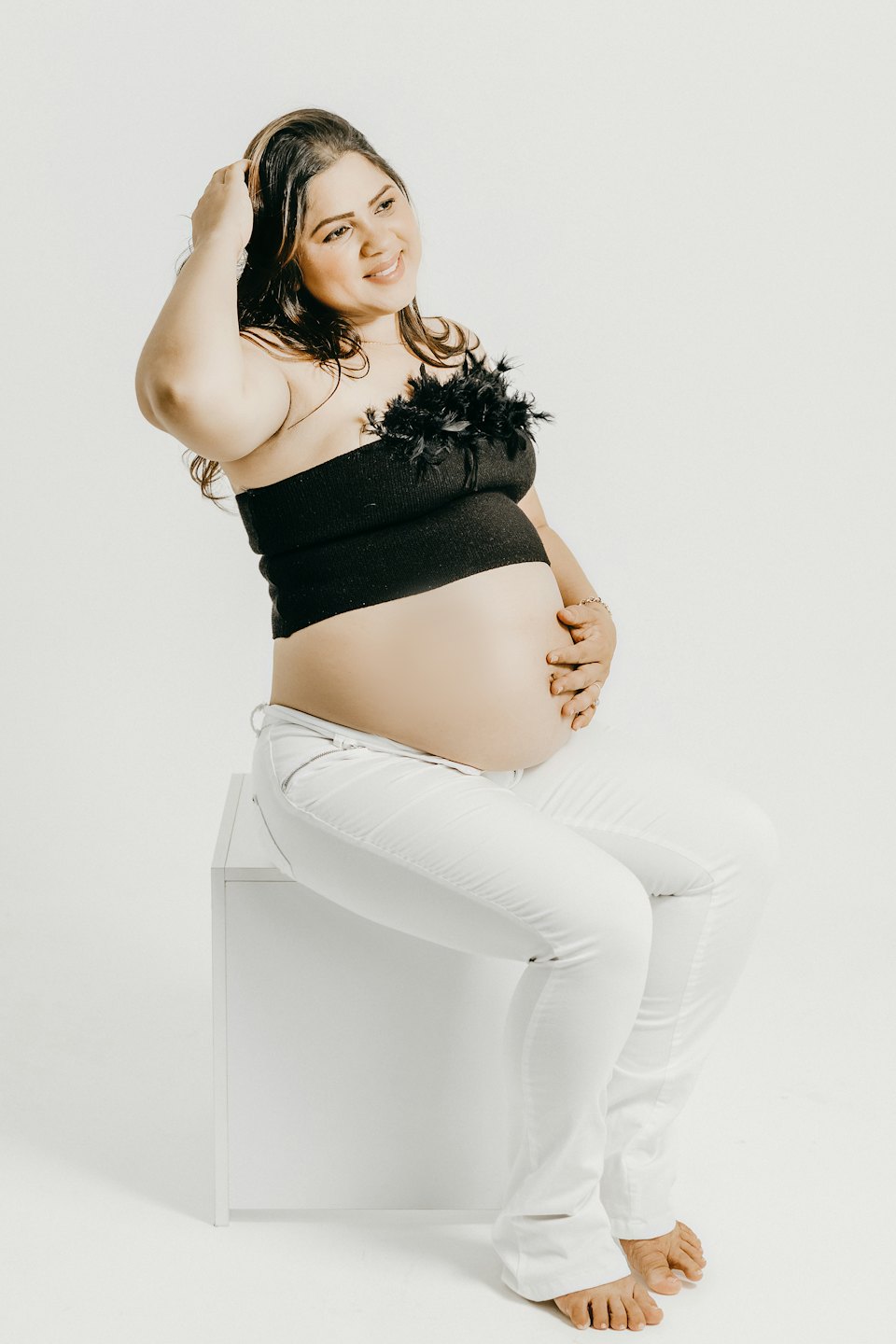 Pregnant woman in a feather top sitting on a block.