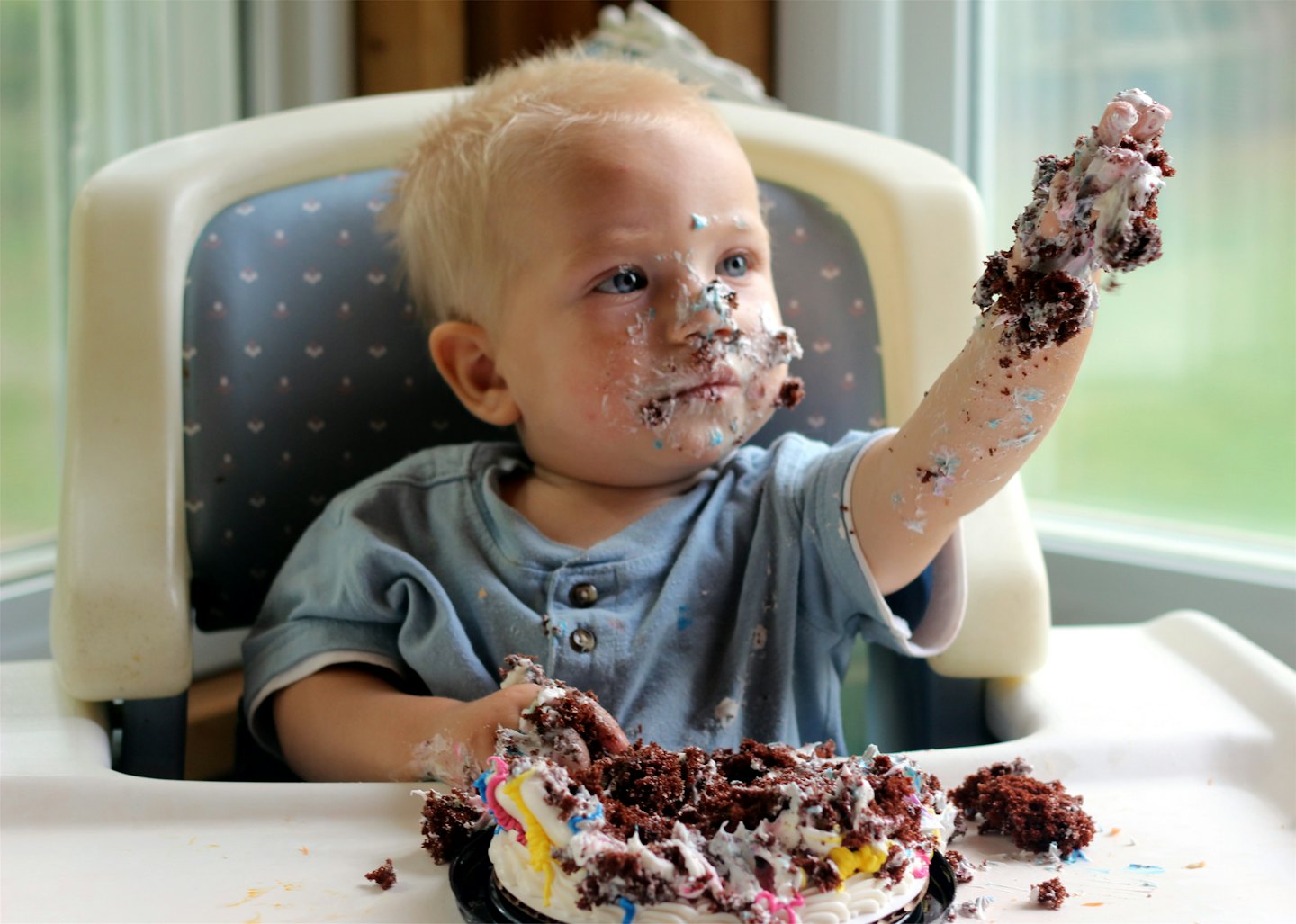 Toddler in a high chair eating a chocolate birthday cake.