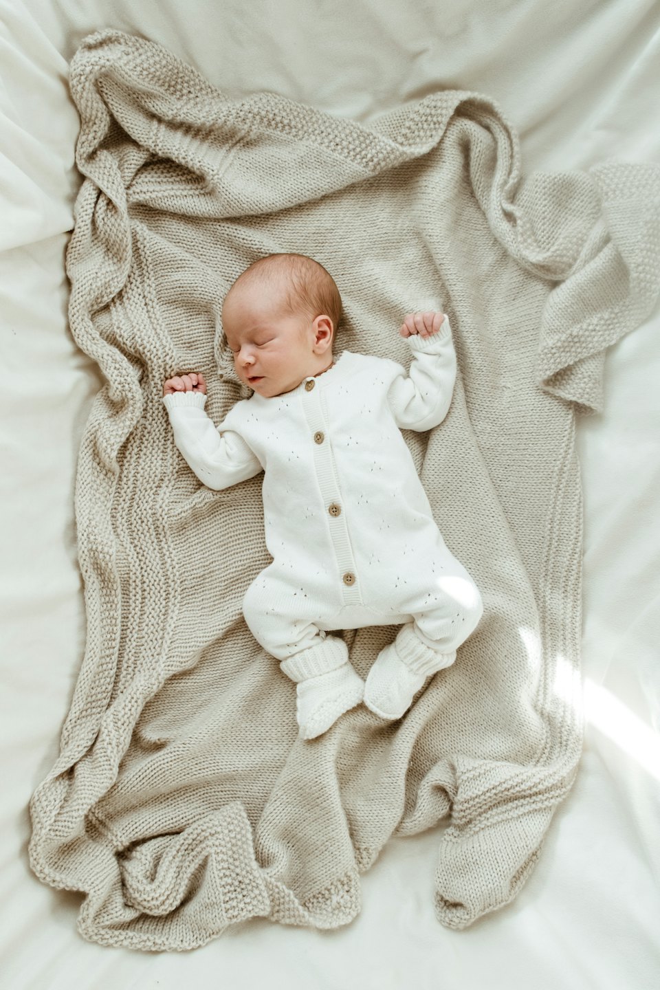 Newborn baby sleeps soundly on a beige knitted blanket.