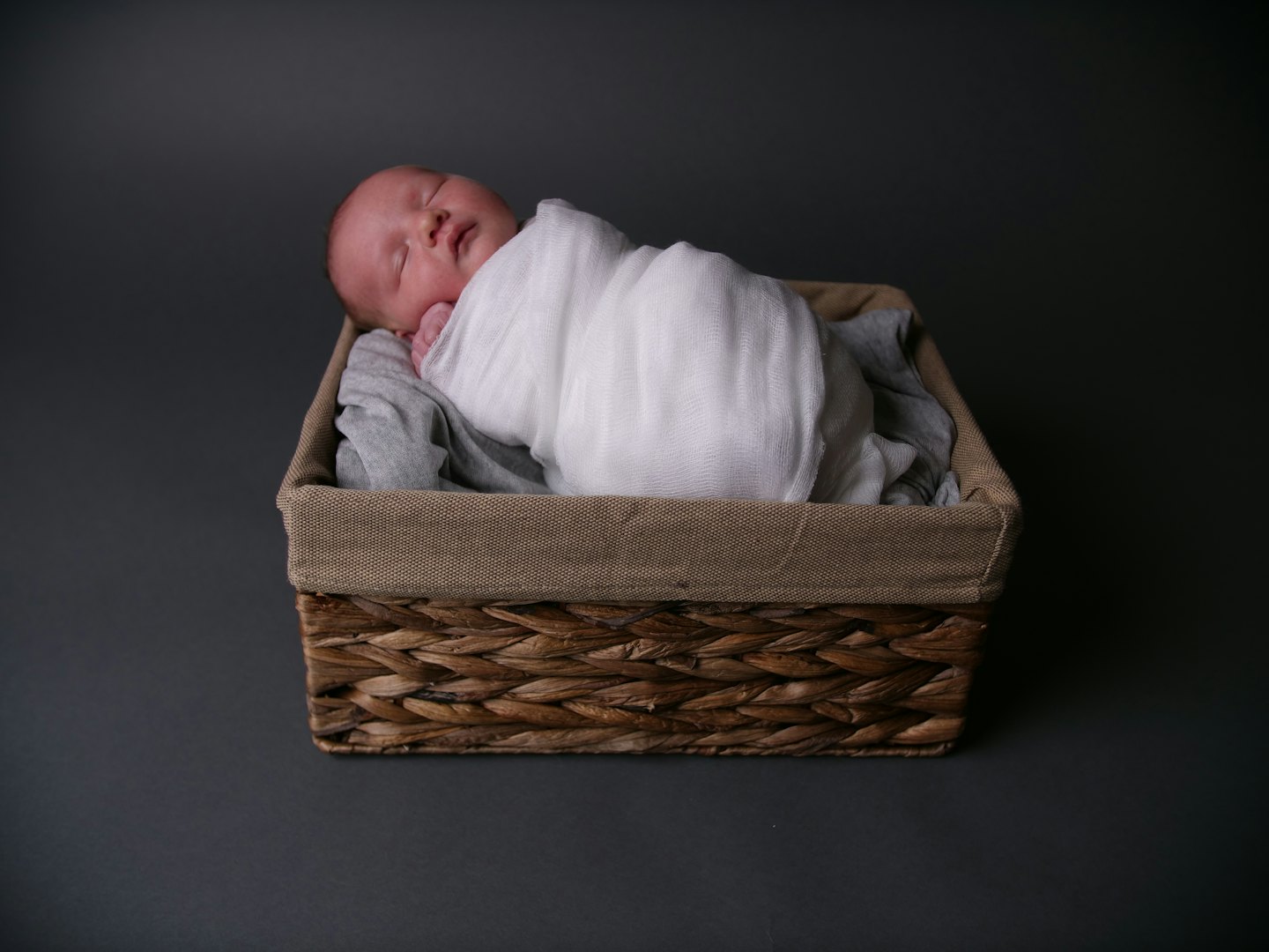 A swaddled newborn sleeping inside a rustic wicker basket.