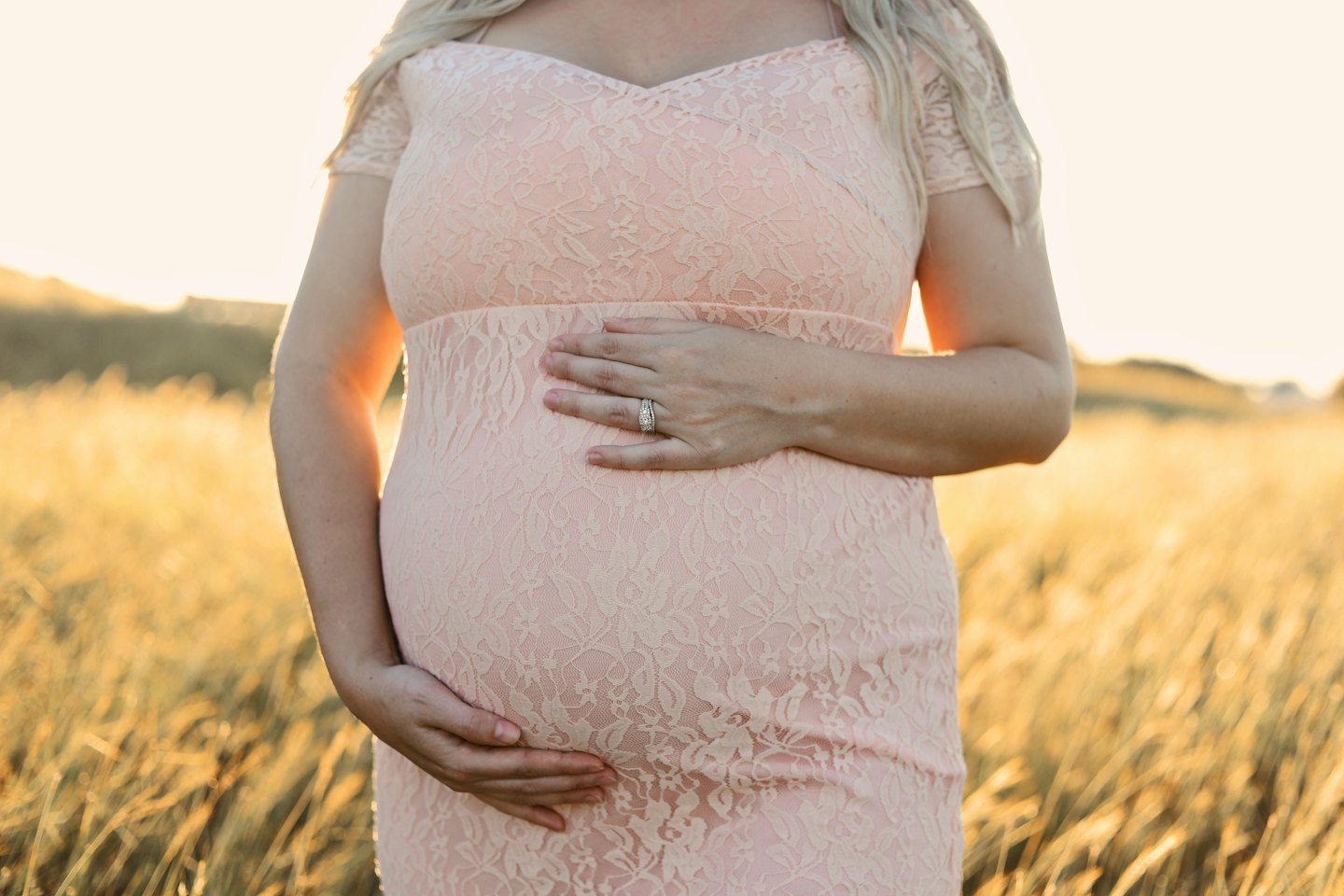 Pregnant woman in pink lace dress in golden field at sunset.